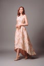 Ginger young woman in golden peach dress with floral print. Calm studio portrait of young lady in long sleeveless evening gown