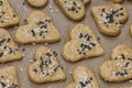 Gingerbread cookie hearts with black and white sesame and sugar on baking paper. The scene of making sweet homemade pastries