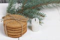 Gingerbread cookies tied with twine. Nearby there is a candle stub and a spruce branch. On boards painted white