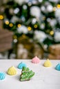 Gingerbread fir tree and meringue on the table in front of defocused lights of Christmas decorated fir tree. Holiday sweets. New Y