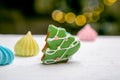 Gingerbread fir tree and meringue on the table in front of defocused lights of Christmas decorated fir tree. Holiday sweets. New Y