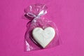 Gingerbread heart decorated with icing in gift plastic bag with ribbon on pink background
