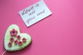 Gingerbread heart with white icing and pink flowers shit of paper on pink background. Love concept. Gift for womans and valentines Royalty Free Stock Photo