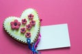 Gingerbread heart with white icing and pink flowers shit of paper on pink background. Love concept. Gift for womans and valentines Royalty Free Stock Photo