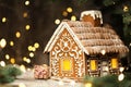 Gingerbread House with Christmas Gift over Shining Garland Lights Background. Xmas Holiday Present Art Decoration. Baked Sweet Royalty Free Stock Photo