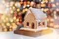 Gingerbread house with white icing over defocused lights of Chrismtas decorated fir tree. Sweet Christmas decoration Royalty Free Stock Photo