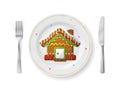 Gingerbread house is on white plate with fork and knife, top view