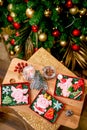 Gingerbread piggy in carton box on the table with fir branches, nuts and berries in front of decorated fir tree, top view. Holiday