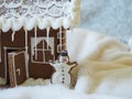 Gingerbread snowman with white icing in front of a gingerbread house