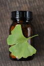 Ginkgo biloba pills .Brown glass jar with homeopathic pills and ginkgo leaves on wooden background . Alternative