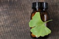 Ginkgo biloba pills .Brown glass jar with homeopathic pills with ginkgo extract and ginkgo leaves on wooden background