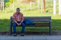 Gipuzkoa, SPAIN-MARCH 22, 2018 : Sad and tired man sitting on wooden bench in park. Old man wear plaid shirt and jeans. Caucasian