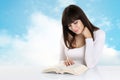 Girl absorbed in reading a book on background with sky clouds