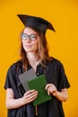 Girl in academic dress and with a diploma in her hands on a yellow background