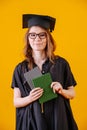Girl in academic dress with diploma in her hands on a yellow background Royalty Free Stock Photo