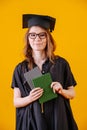 Girl in academic dress with diploma in her hands on a yellow background