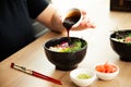Girl adding teriyaki sauce to Poke salad. Dressing salad with sauce in a restaurant or cafe. Royalty Free Stock Photo