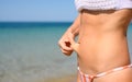 A girl against the background of the sea tightens the skin in the abdomen to check the level of subcutaneous fat