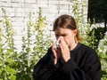 A girl with allergies sneezes into a handkerchief on the street among flowers, the concept of allergic reactions Royalty Free Stock Photo