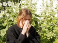 A girl with allergies sneezes into a handkerchief on the street among flowers, the concept of allergic reactions