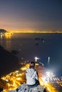 A girl alone climbed to the top of Mount. There are beautiful lights coming from the roads and buildings. Night view of Nerano bay