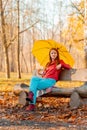 Girl alone sits under an umbrella in an autumn park on a bench cut from a log Royalty Free Stock Photo