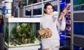 Girl in aquarium shop choosing brown petrous wood for aquarium decoration