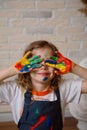 A girl artist in a creative workshop covers her face with her hands stained with paint on the background of a brick wall. Royalty Free Stock Photo