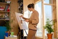 Girl artist draws on an easel at home, molubert stands at the window