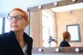 Girl artist in the dressing room. Sitting in front of a mirror with lamps. In the eyes of beautiful stylish glasses Royalty Free Stock Photo