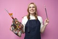 Girl artist holds brushes and a palette and smiles on a pink background, student of art school, profession of an artist