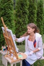 Girl artist paints picture and sits on chair at easel sides of t Royalty Free Stock Photo