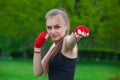 The girl the athlete, the boxer, in the park also gives the hand compressed in a fist forward with the reeled sports, red bandage.