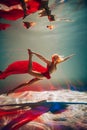 A girl with an athletic figure, with red material and light underwear, in a ballet pose underwater Royalty Free Stock Photo