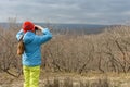 A girl in an autumn day looks through binoculars from the mountain, back view