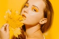 Girl with autumn leaves and red makeup, grimaces and has fun. Autumn photo on a yellow background. Fashion photo model Royalty Free Stock Photo