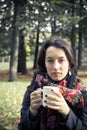 Girl in an autumn part with a white cup of hot drink