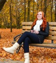 Girl in autumn season listen music on audio player with headphones, sit on bench in city park, yellow trees and fallen leaves Royalty Free Stock Photo