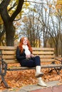 Girl in autumn season listen music on audio player with headphones, sit on bench in city park, yellow trees and fallen leaves Royalty Free Stock Photo