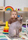 Girl baby with sphinx cat playing with toys indoors