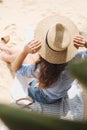 The girl from the back in the hat sits on the sand