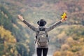 Girl with a backpack and a hat standing on a hill. Hands raised up. River and mountains below. Back view Royalty Free Stock Photo