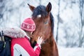 Girl with a backpack hugging with a horse in winter time. Wonderful winter weather with falling snow. The atmosphere of a winter h Royalty Free Stock Photo