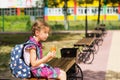 Girl with a backpack sitting on a bench and eating a pie near the school. A quick snack with a bun, unhealthy food, lunch from Royalty Free Stock Photo
