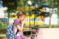 Girl with a backpack sitting on a bench and eating a pie near the school. A quick snack with a bun, unhealthy food, lunch from Royalty Free Stock Photo