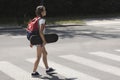 Girl with backpack and skateboard walking through crosswalk to the school Royalty Free Stock Photo