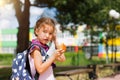 Girl with a backpack take off the medical mask and eating pie near the school. A quick snack with a bun, unhealthy food, lunch Royalty Free Stock Photo