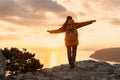 Girl with backpack on top of mountain at sunset with raised arms