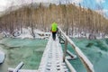 Girl backpacker walking on a bridge over a frozen turquoise ice river in the winter forest in the mountains Royalty Free Stock Photo