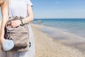 Girl with bag in hands is standing onear sea. View of the gray T-shirt and bag with big blue stick
